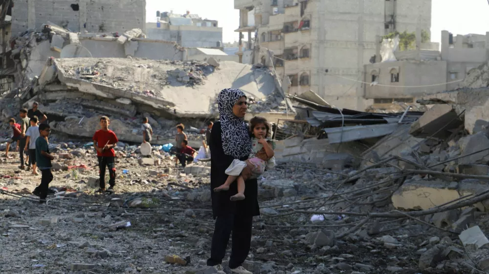 A Palestinian woman carries a child, as they inspect the site of an overnight Israeli strike on a house, in Gaza City, August 26, 2025. REUTERS/Ebrahim Hajjaj