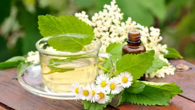 Chamomile, lemon balm and elderberry herbal tea in a glass cup, with essential oil in a bottle arranged on a wooden desk / Foto: Miloscirkovic