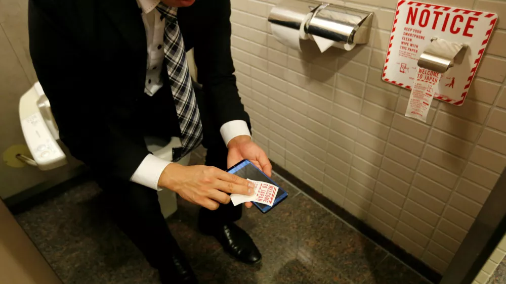 A man demonstrates a toilet roll for wiping smartphones, installed by Japanese mobile phone company NTT Docomo, in a high-tech bathroom equipped with bidet and heated seat at Narita international airport in Narita, Japan, December 28, 2016. REUTERS/Toru Hanai