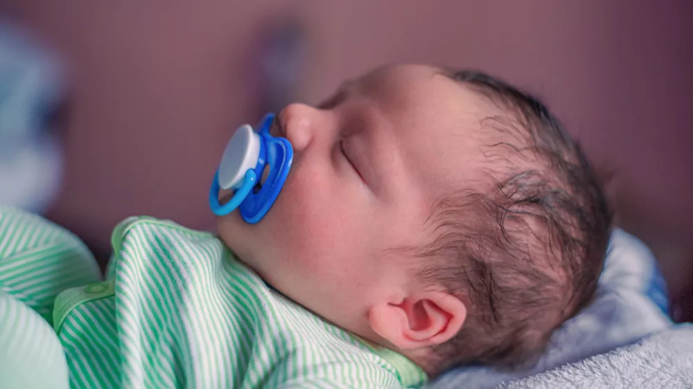 Face profile portrait of a sleeping newborn baby with a pacifier in his mouth