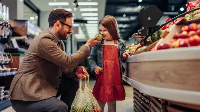 Father and daughter smiling apple, tasting quality while buying groceries in market