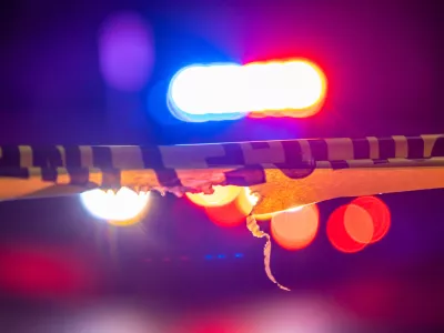 A defocused police car sits behind crime scene tape with flashing lights at night.