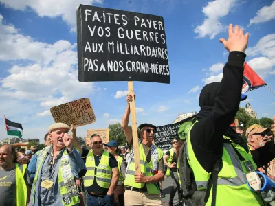 Demonstranti med leto&scaron;njimi delavskim praznikom. Na transparentu pi&scaron;e: Za va&scaron;e vojne naj plačajo milijarderji, ne na&scaron;e babice.