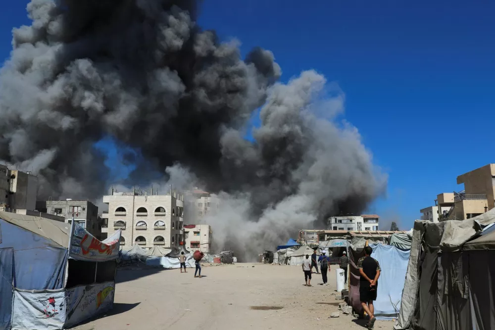 Palestinians look at smoke rising from an evacuated residential building which was housing displaced Palestinians after it was hit by an Israeli air strike, in Gaza City, September 14, 2025. REUTERS/Ebrahim Hajjaj