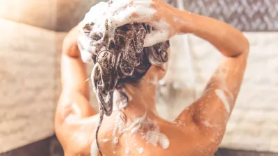 Back view of beautiful naked young woman is using shampoo while taking shower in bathroom / Foto: Vadimguzhva
