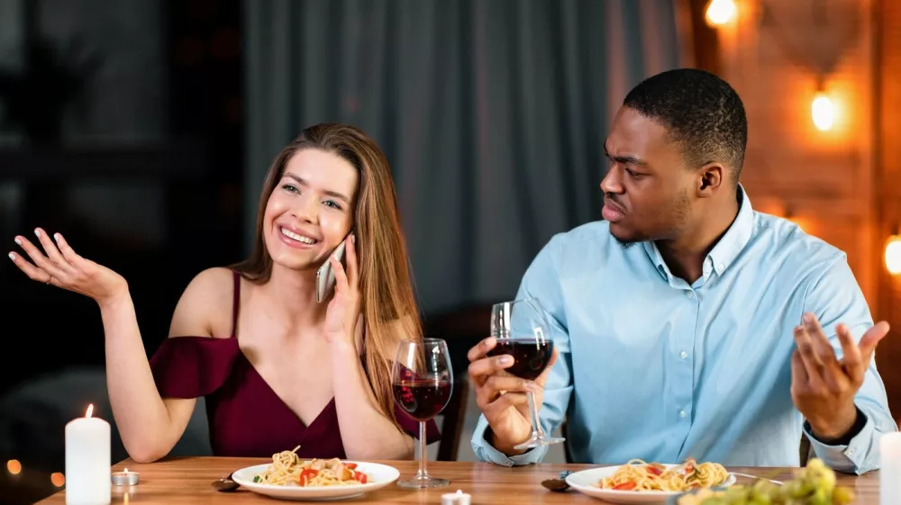Annoyed African Man Looking At His Girlfriend Talking On Mobile Phone During Romantic Dinner In Restaurant, Complaining About Her Cellphone Addiction. Interracial Couple Having Communication Problems,Image: 1017031699, License: Royalty-free, Restrictions:, Model Release: no