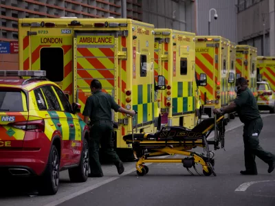 Paramedics push a trolley next to a line of ambulances outside the Royal London Hospital in the Whitechapel area of east London, Thursday, Jan. 6, 2022. Health authorities across the U.K. simplified COVID-19 testing requirements on Wednesday, a move designed to cut isolation times for many people and that may ease the staffing shortages that are hitting public services amid an omicron-fueled surge in coronavirus infections. A string of National Health Service local organizations have declared "critical incidents" in recent days amid staff shortages. (AP Photo/Matt Dunham)