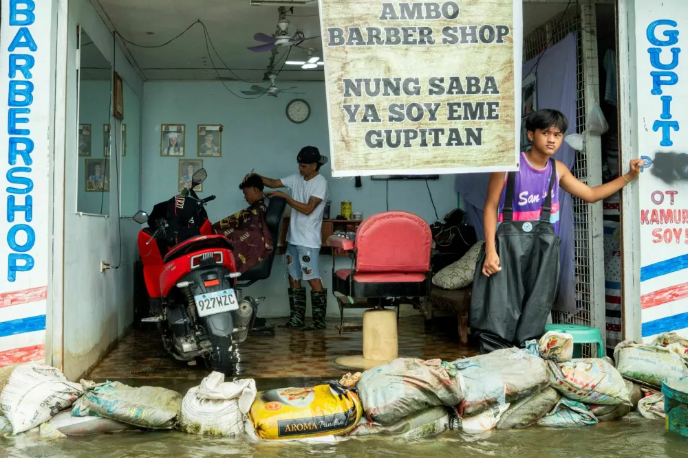 Edwardo Puno cuts a customer's hair in his flooded barbershop, following heavy rains intensified by Super Typhoon Ragasa, in Apalit, Pampanga province, Philippines, September 23, 2025. REUTERS/Lisa Marie David