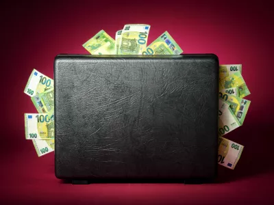 A briefcase overflowing with euro banknotes. Concept studio shot on illuminated burgundy red background with dark vignette / Foto: Smileus