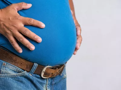 Overweight or fat adult man in very tight jeans on a gray background. Healthcare, medicine concept.Simbo