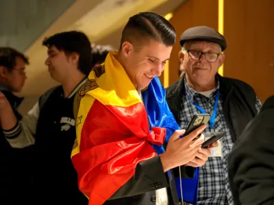 A supporter of the pro-EU Party of Action and Solidarity (PAS) draped in the Moldovan flag smiles as he checks partial results on a phone after the polls closed for the parliamentary election, in Chisinau, Moldova, Sunday, Sept. 28, 2025. (AP Photo/Vadim Ghirda)