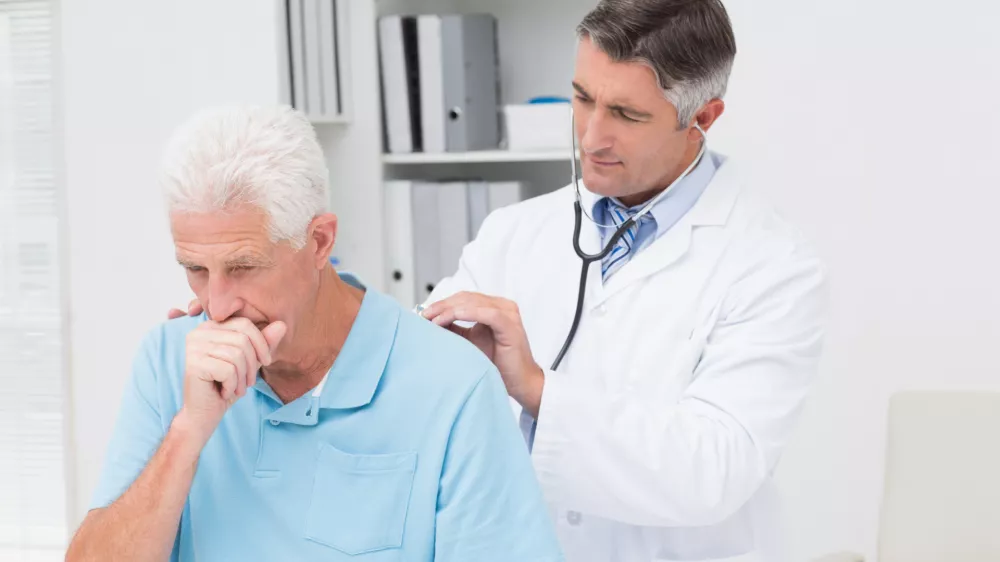 Male doctor examining coughing senior patient in clinic