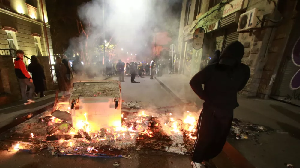 A demonstrator stands behind a burning barricade not far from a police line during an opposition rally in the city center of Tbilisi, Georgia, on Sunday, Oct. 5, 2025, boycotting the municipal elections and calling for the release of political opponents. (AP Photo/Zurab Tsertsvadze)