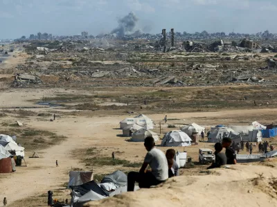Palestinians look on as smoke rises following explosions in Gaza City, as seen from central Gaza Strip October 5, 2025. REUTERS/Mahmoud Issa