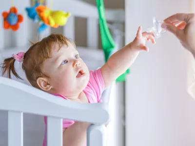 Little girl pulls her hand to the dummy, standing in a baby crib