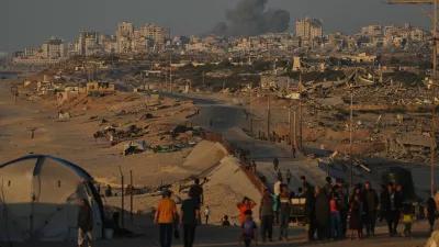 Displaced Palestinians walk along the coastal road, backdropped by smoke rising into the sky after an Israeli military strike in Gaza City, as seen from the central Gaza Strip, Wednesday, Oct. 8, 2025. (AP Photo/Abdel Kareem Hana)