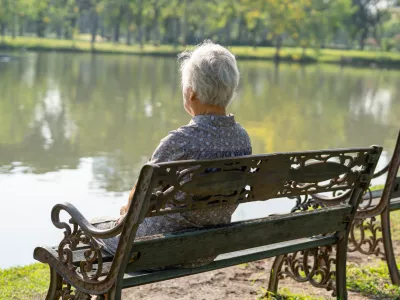 Asian elderly woman depressed and sad sitting back on bench in autumn park.