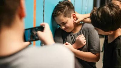 A young boy is being bullied by peers at school. The boy is upset as another boy grabs his neck. A third boy records the bullying incident on his phone. Bullying of teenager in high scool.