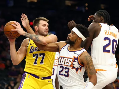 Oct 14, 2025; Phoenix, Arizona, USA; Los Angeles Lakers guard Luka Doncic (77) grabs a rebound against Phoenix Suns guard Jordan Goodwin (23) and forward Rasheer Fleming (20) during an NBA preseason game at Mortgage Matchup Center. Mandatory Credit: Mark J. Rebilas-Imagn Images