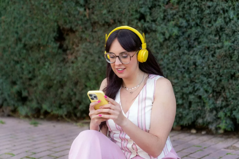 Woman wearing yellow headphones enjoying music and using mobile phone app in a park,Image: 1001571904, License: Royalty-free, Restrictions:, Model Release: no