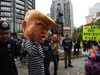 A protester dressed as President Donald Trump in chains and a prison jumpsuit looks at another holding a sign referencing the Epstein files as people take part in a "No Kings" protest Saturday, Oct. 18, 2025, in Seattle. (AP Photo/Lindsey Wasson)
