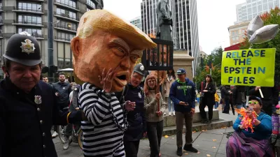 A protester dressed as President Donald Trump in chains and a prison jumpsuit looks at another holding a sign referencing the Epstein files as people take part in a "No Kings" protest Saturday, Oct. 18, 2025, in Seattle. (AP Photo/Lindsey Wasson)