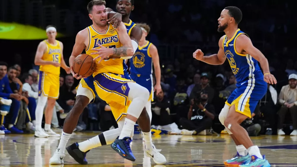 Los Angeles Lakers' Luka Dončić, left, is defended by Golden State Warriors guard Jonathan Kuminga during the first half of an NBA basketball game Tuesday, Oct. 21, 2025, in Los Angeles. (AP Photo/Ethan Swope)