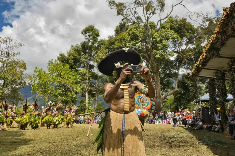 Paiya Village, Western Highlands Province, Papua New Guinea - August 16, 2024: Man of Edgan tribe, wearing the characteristic big hat and traditional costume, is taking pictures of tourists attending the rehearsals for the Sing Sing festival with his mobile.Engan is one of the largest Papuan tribes. / Foto: Mwayout