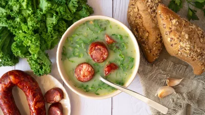 Portuguese style soup called Caldo Verde, bread, Cabbage julienne, and chorizo sausage on a white wooden Table. Flat lay / Foto: Iggi_boo