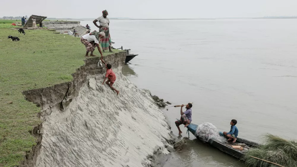 Kosim Uddin, 50, receives fish from a boy after making a purchase, on an island in the Brahmaputra River where he recently relocated his house due to erosion, in Kurigram, Bangladesh, October 29, 2025. REUTERS/Mohammad Ponir Hossain