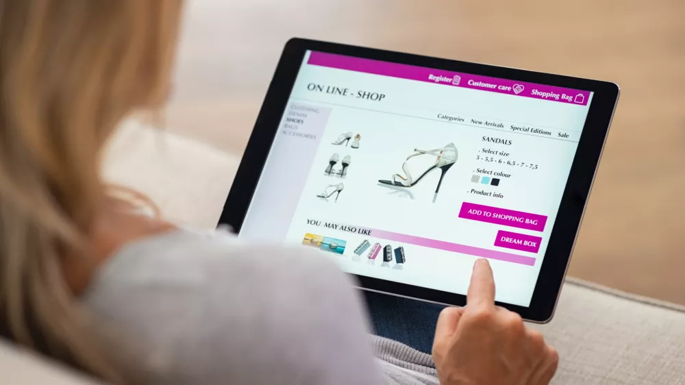 Closeup of woman doing online shopping on digital tablet at home. Rear view of woman hand touching screen while selecting shoes on ecommerce portal. Lady use e-commerce webshop to buy shoes.