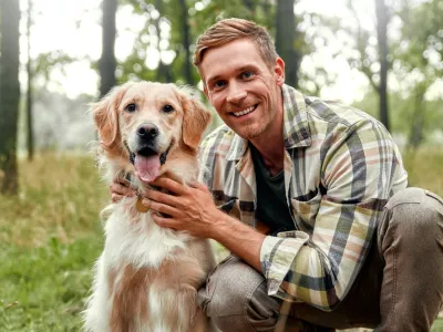 A cheerful man enjoys a delightful moment with his playful golden retriever in a lush forest, capturing joy and companionship in nature, ideal for pet lovers and outdoor enthusiasts