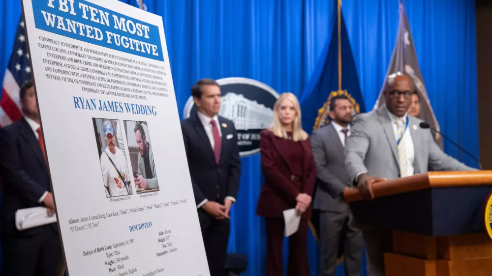 Akil Davis, assistant director in charge of the FBI's Los Angeles Field Office, looks at a wanted poster for Canadian fugitive Ryan James Wedding as he speaks with reporters during a news conference at the Department of Justice, Wednesday, Nov. 19, 2025, in Washington. (AP Photo/Mark Schiefelbein)