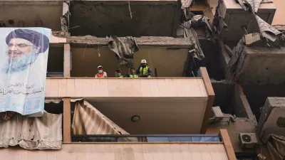 A large banner depicting Hezbollah's late leader Hassan Nasrallah hangs from a damaged balcony as civil defense workers clear the rubble in a residential building that was hit in Sunday's Israeli airstrike killing Hezbollah's chief of staff, Haytham Tabtabai in the southern suburb of Hareit Hreik, Beirut, Lebanon, Monday, Nov. 24, 2025. (AP Photo/Hassan Ammar)