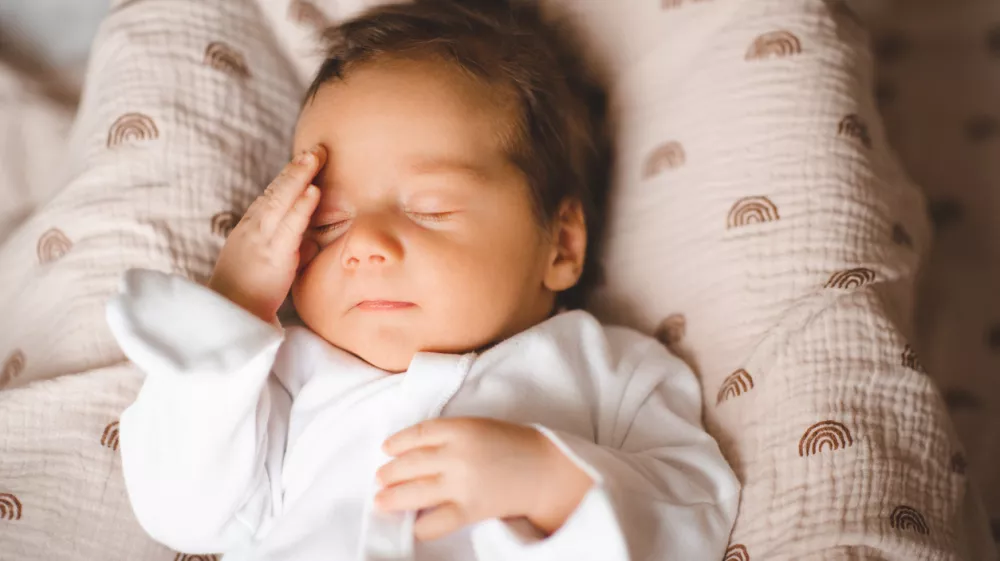 Infant baby boy 2-3 months old with headache and pain touching head in bed closeup. Childhood. Good morning.