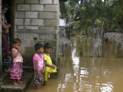 A family stands near their flooded home in Batticaloa district, about 320 km (199 miles) east of Colombo, February 6, 2011. Heavy rain triggered flooding in Sri Lanka that killed at least eleven people and is threatening up to 90 percent of the island nation's staple rice crop, heightening concerns over supply shocks and higher inflation, officials said on Sunday. REUTERS/Stringer (SRI LANKA - Tags: DISASTER ENVIRONMENT)