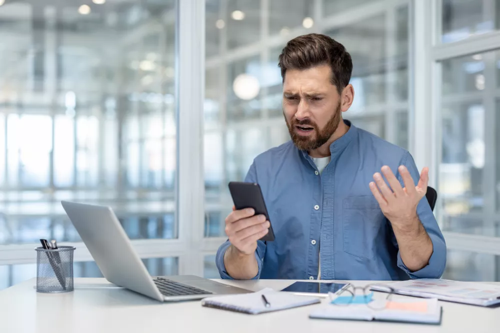 Upset man reading online notification message on phone, worker at workplace inside office holding smartphone in hands, got app error, and account blocked. / Foto: Liubomyr Vorona