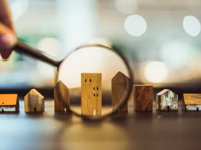 Hand holding magnifying glass and looking at house model, house selection, real estate concept.