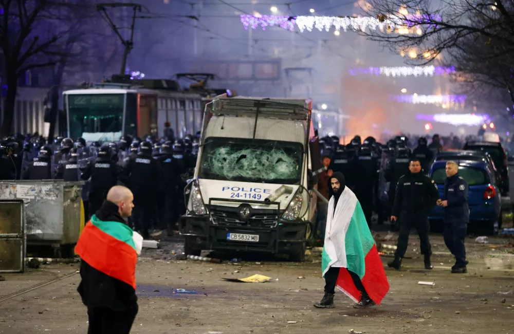 Police stand in formation as protesters walk covered by Bulgarian flags during a rally against austerity measures in next year's draft budget, in Sofia, Monday, Dec 1, 2025. (AP Photo/Valentina Petrova)