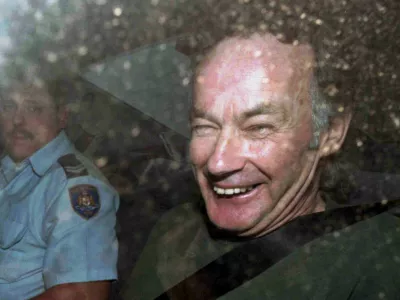 FILE - In this Nov. 4, 1997, file photo, Ivan Milat smiles in a police car after attending a court in Sydney, Australia. Milat, whose grisly serial killings of young backpackers horrified Australians in the early '90s, died in a Sydney prison on Sunday, Oct. 27, 2019, prison authorities said. He was 74. (AP Photo/Rick Rycroft, File)