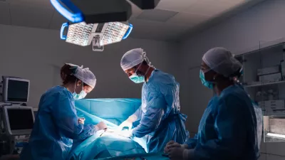 An intricate surgical procedure in progress with healthcare professionals in full surgical gear, under bright operating room lights, emphasizing the modern medical equipment and organization. / Foto: Zamrznutitonovi