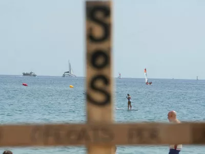 People are seen sailing behind a wooden cross placed by lifeguards, which has the word "drowned" written on it, as lifeguards protest on the shortage of personnel and precarious instalments along the beaches, following more than 700 drownings last year across Spain, according to the Royal Spanish Lifeguard and First Aid Federation, in Barcelona, Spain August 1, 2025. REUTERS/Bruna Casas