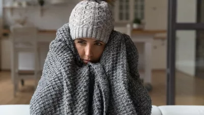 Dull young hispanic woman save herself from freezing wear winter clothes muffle up in blanket think of buying radiator heater. Shivering young lady sit on sofa in plaid ponder on much too cold at home / Foto: Fizkes