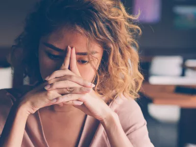 Closeup of sad young Asian woman at cafe leaning head on clasped hands and staring into vacancy. Tired freelancer feeling burnout. Stress and bad news concept / Foto: Mangostar_studio