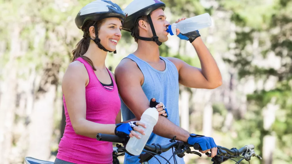 Young couple holding water bottle while riding bicycle at forest / Foto: Wavebreakmedia