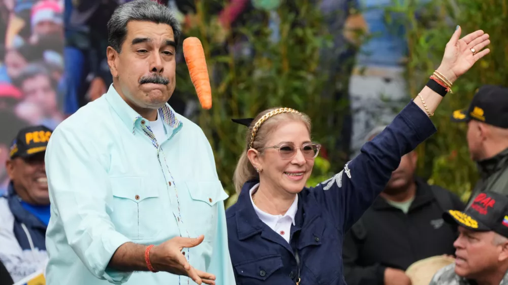 President Nicolas Maduro tosses a carrot next to his wife Cilia Flores during a rally marking the anniversary of the Battle of Santa Ines, which took place during Venezuela's 19th-century Federal War, in Caracas, Venezuela, Wednesday, Dec. 10, 2025. (AP Photo/Ariana Cubillos)