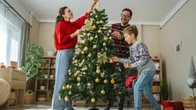 Happy family decorating beautiful christmas tree with golden and white ornaments and warm lights, enjoying their time together during winter holidays