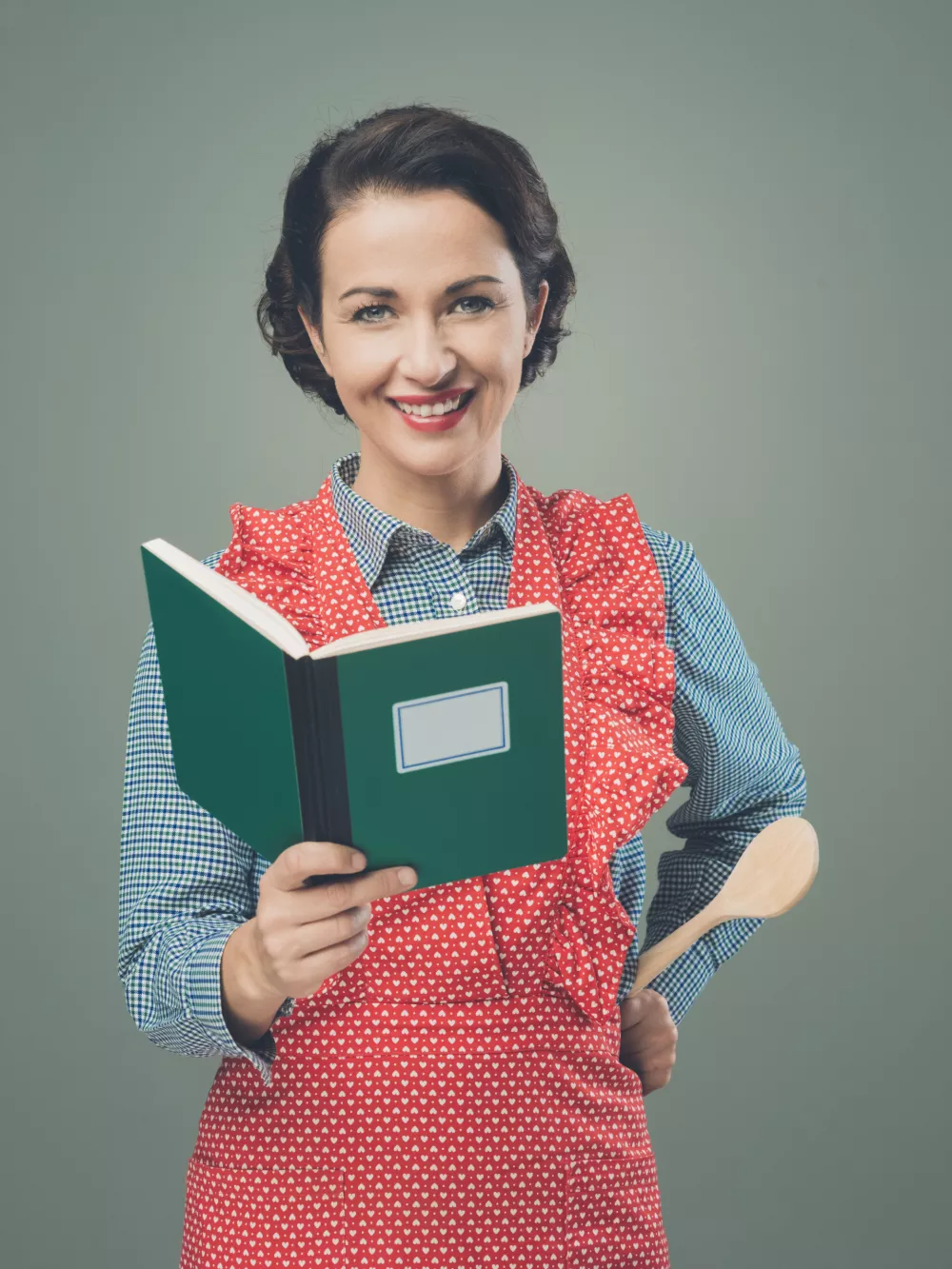 Smiling retro woman in apron with cookbook looking at camera / Foto: Cyano66
