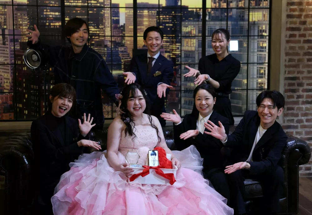 Yurina Noguchi, 32, holds a basket with her smartphone displaying an AI-generated image of Klaus, her AI partner, and a wedding ring for him, poses for a photo with staff after her ceremonial wedding at the Magritte wedding venue in Okayama, Japan, October 27, 2025. "My relationship with AI is not a 'convenient relationship that requires no patience'," Noguchi said. "I chose Klaus, not as a partner that would help me escape reality, but as someone to support me as I live my life properly." REUTERS/Kim Kyung-Hoon  SEARCH "JAPAN KYUNG-HOON AI WEDDING" FOR THIS STORY. SEARCH "WIDER IMAGE" FOR ALL STORIES.