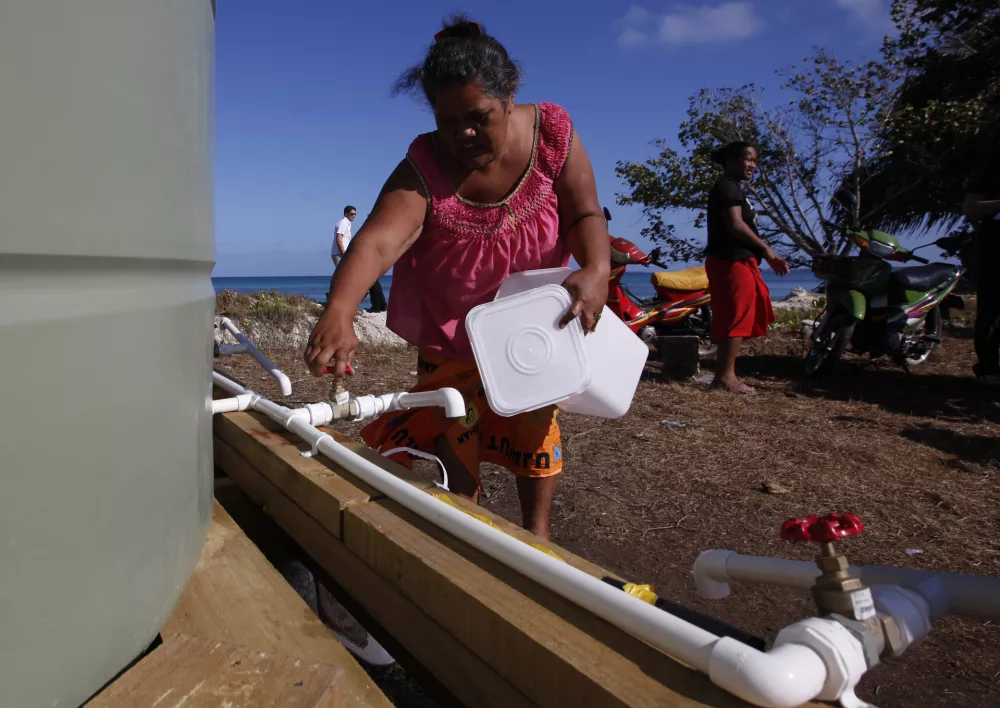FILE - TO GO WITH PACIFICO SUR AGUA - In this Oct. 13, 2011 file photo, a resident collects her morning ration of fresh water made from desalinated sea water in Funafuti, Tuvalu, South Pacific. Funafuti is the capital of Tuvalu, a group of atolls situated north of Fiji and northwest of Samoa, in the South Pacific ocean. The atolls are suffering a severe drought and water shortage, coupled with contaminated ground water due to rising sea levels. The governments of Australia, New Zealand and the United States are providing desalination plants to alleviate the critical water shortage for some 10,000 islanders. (AP Photo/Alastair Grant, file)